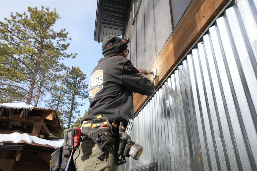 Woods Heating and Cooling technician installing ductwork on exterior of custom home in Deadwood, SD.