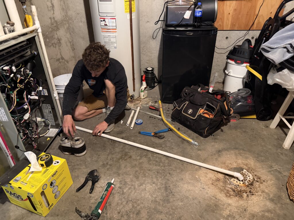 Woods Heating and Cooling technician running a PVC condensate drain line for a new high-efficiency furnace in an older home's basement in Lead, SD.