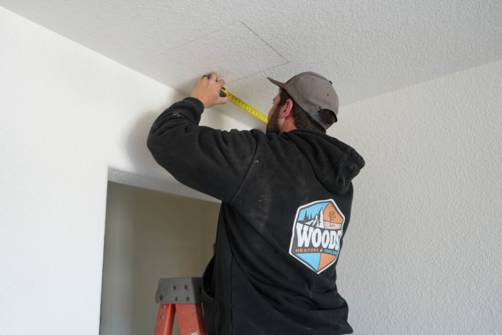 Woods Heating & Cooling HVAC contractor measures ceiling for cutout for vent in new construction HVAC services.